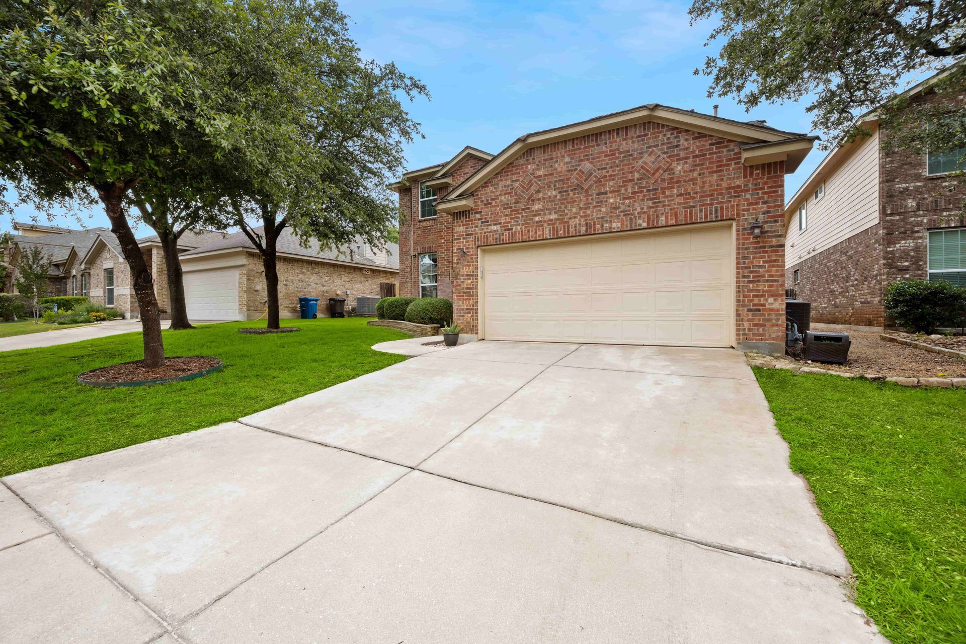 Suburban brick house with a two-car garage, concrete driveway, and green front lawn under a blue sky