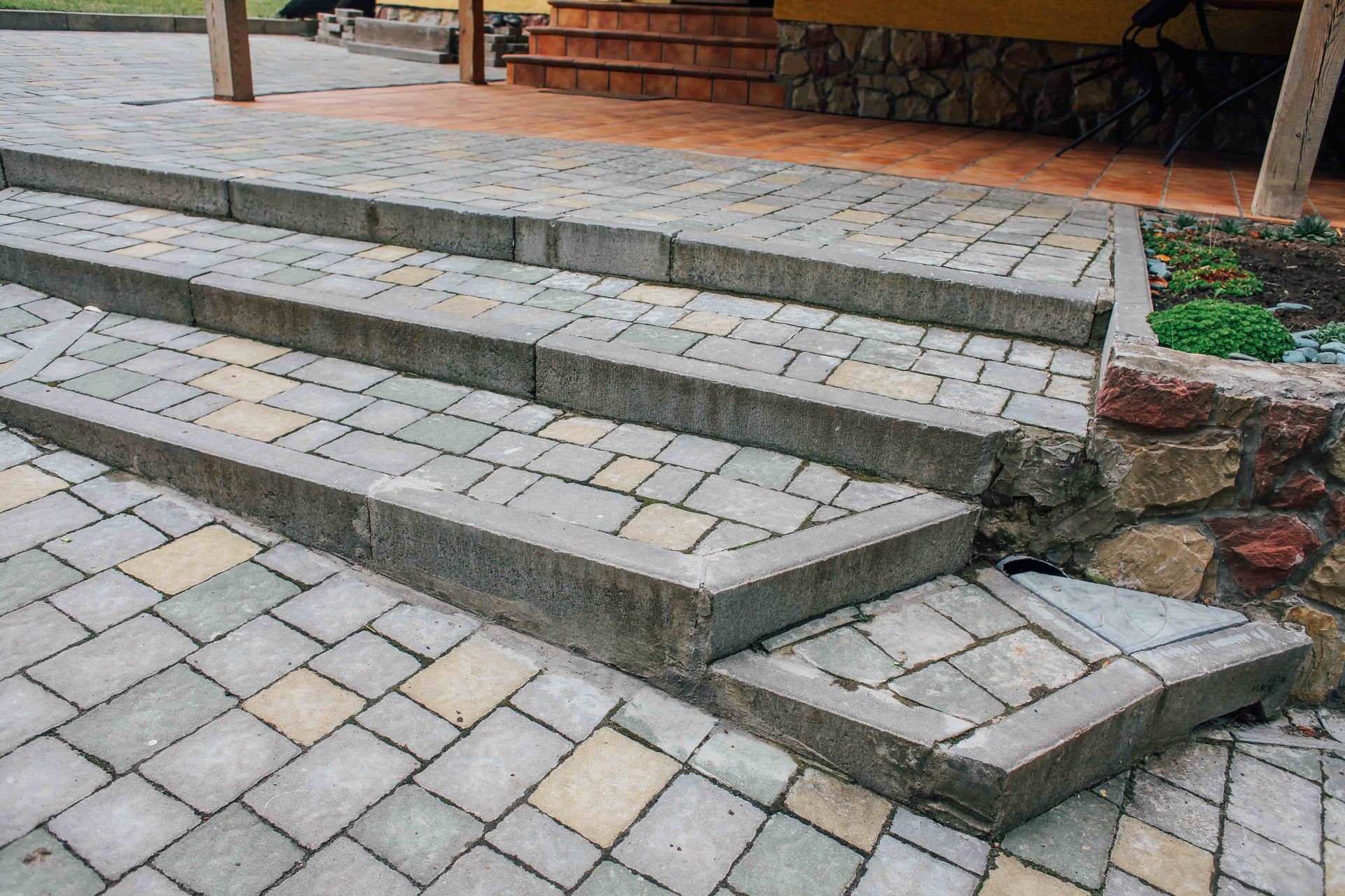Stone outdoor steps leading to a patio, with a paver walkway and stone-edged garden bed