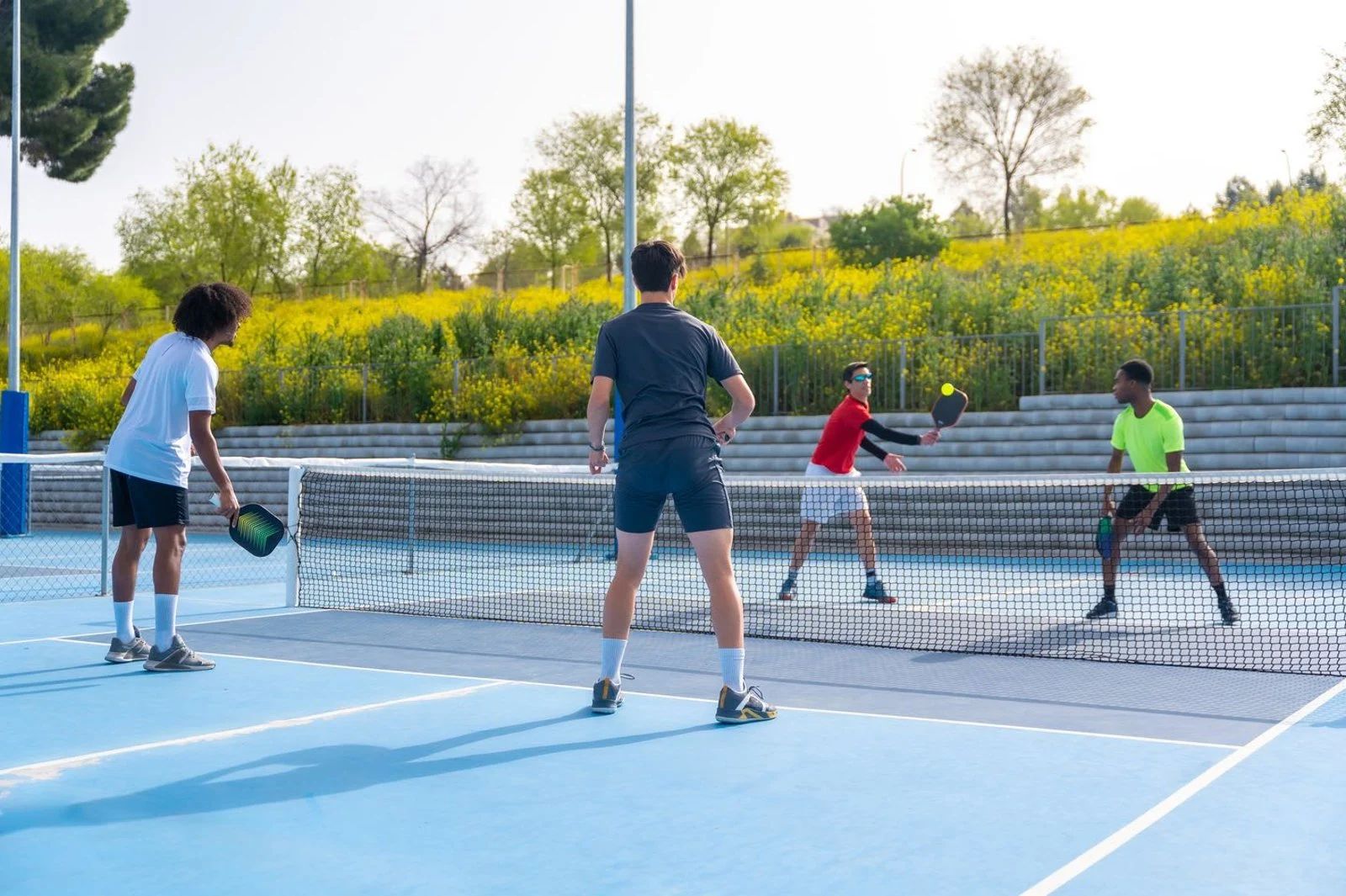 Four people playing pickleball on an outdoor blue court near a net under a clear sky