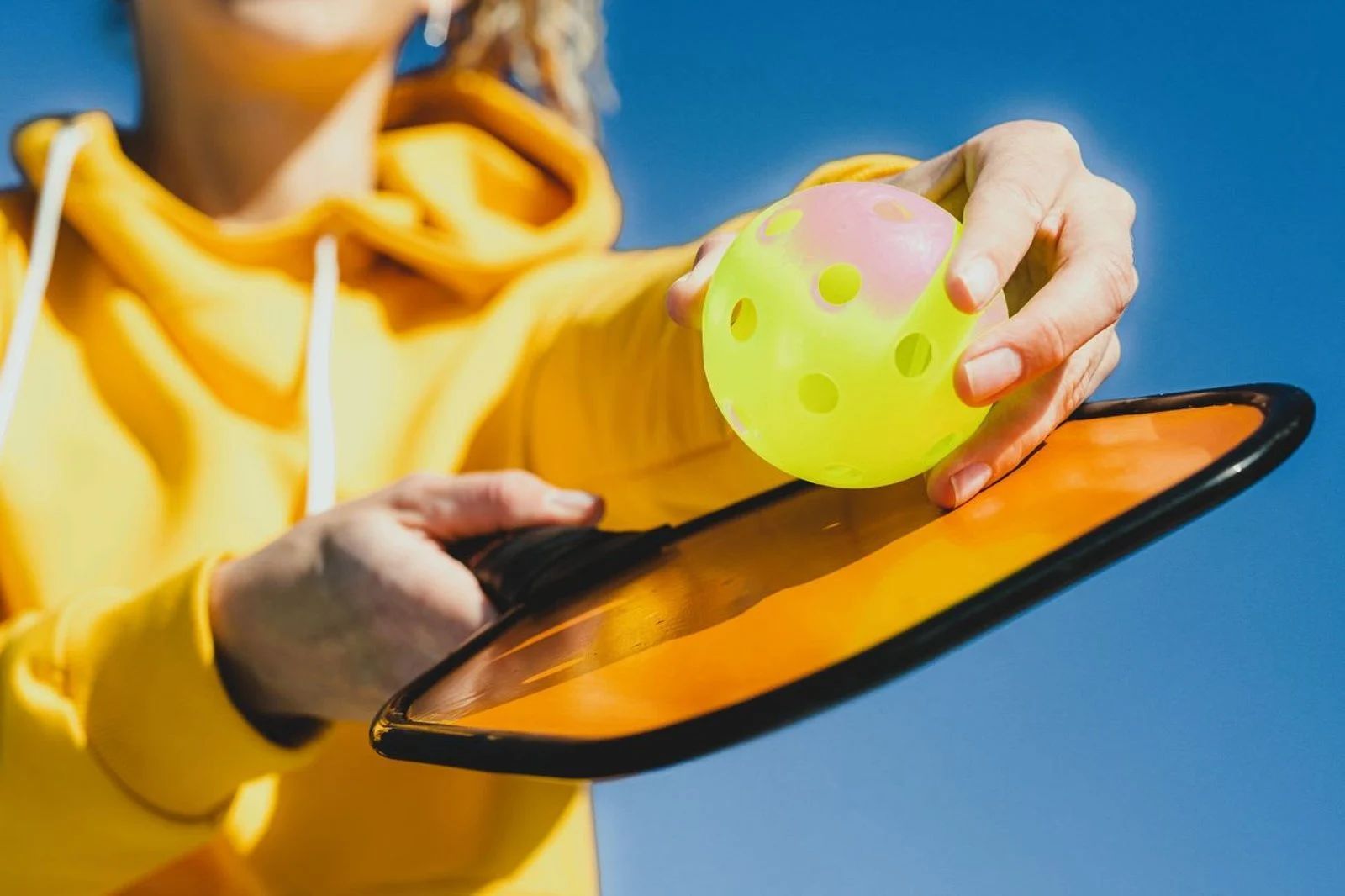 Person in yellow shirt holding a black tablet and green ball against a blue sky