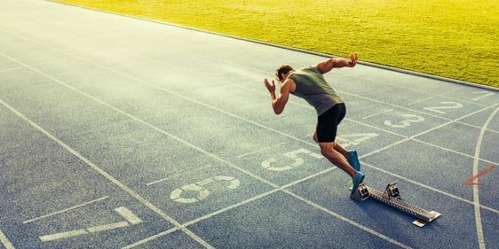 Sprinter launching from blocks on a track with lane markings, starting a race.
