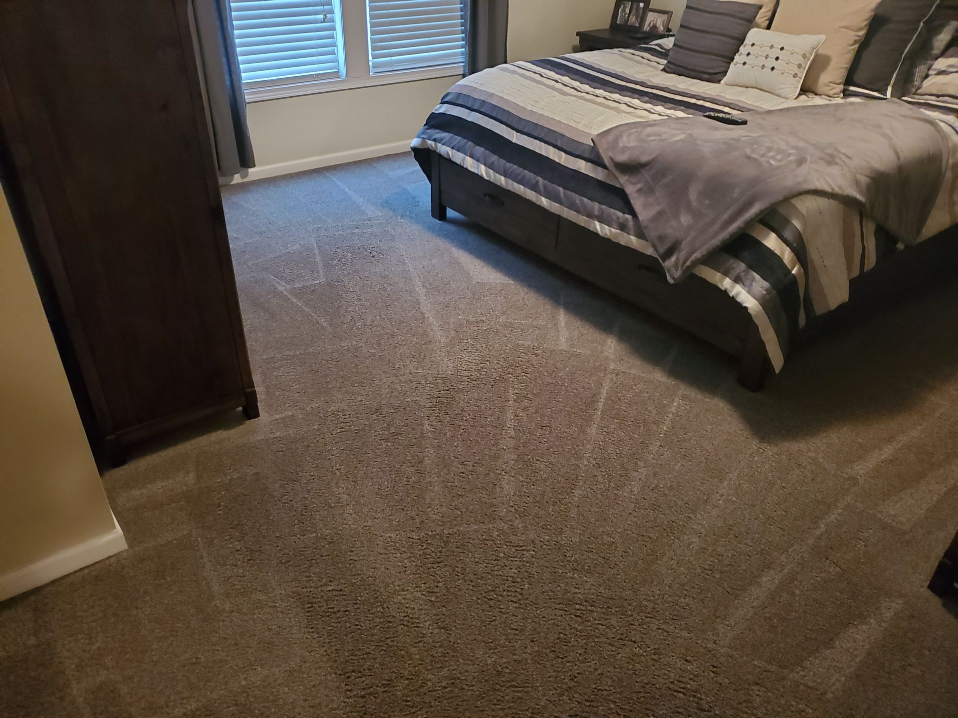 Bedroom with gray carpet, bed with striped comforter, and a dark wooden dresser.