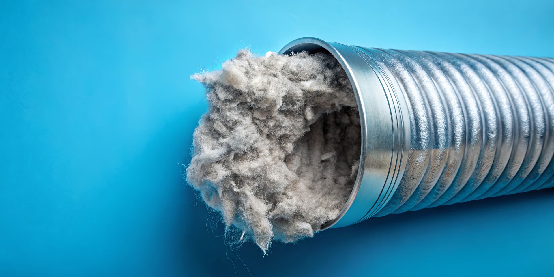 A dryer vent clogged with gray lint against a blue background.