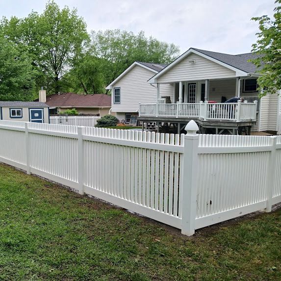 White vinyl fence around a gray house with a porch in a grassy suburban yard