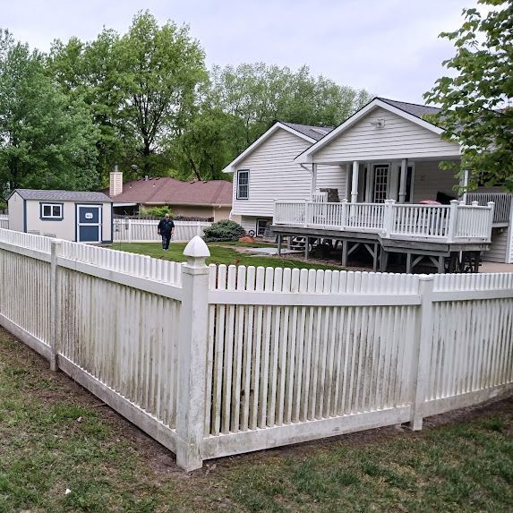 White vinyl fence around a gray house with porch and shed in a grassy yard