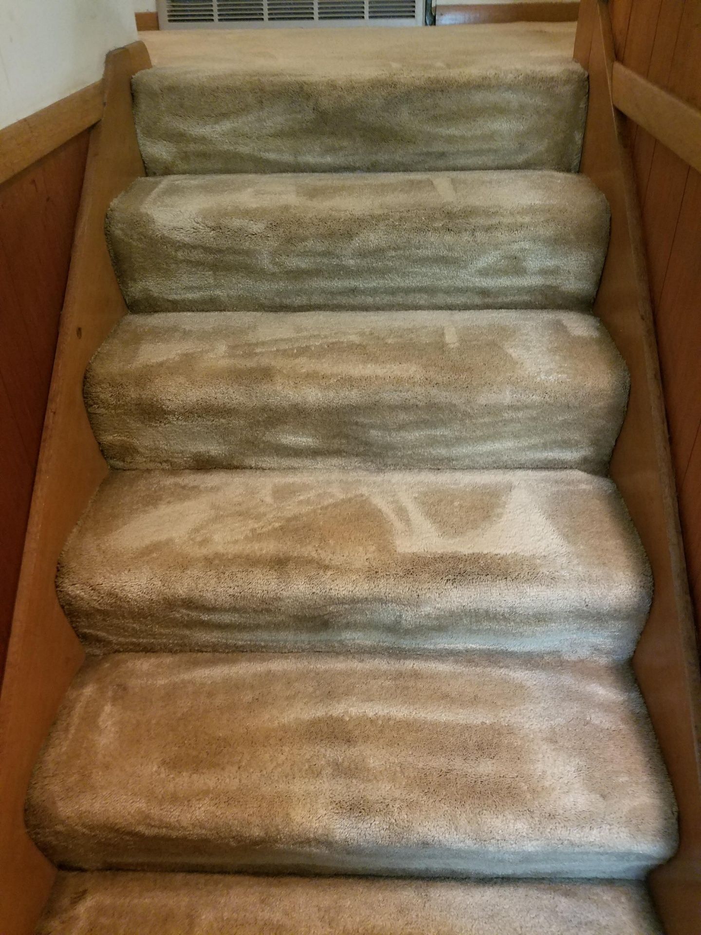 Carpeted staircase with visible wear; beige color. Wooden frame.