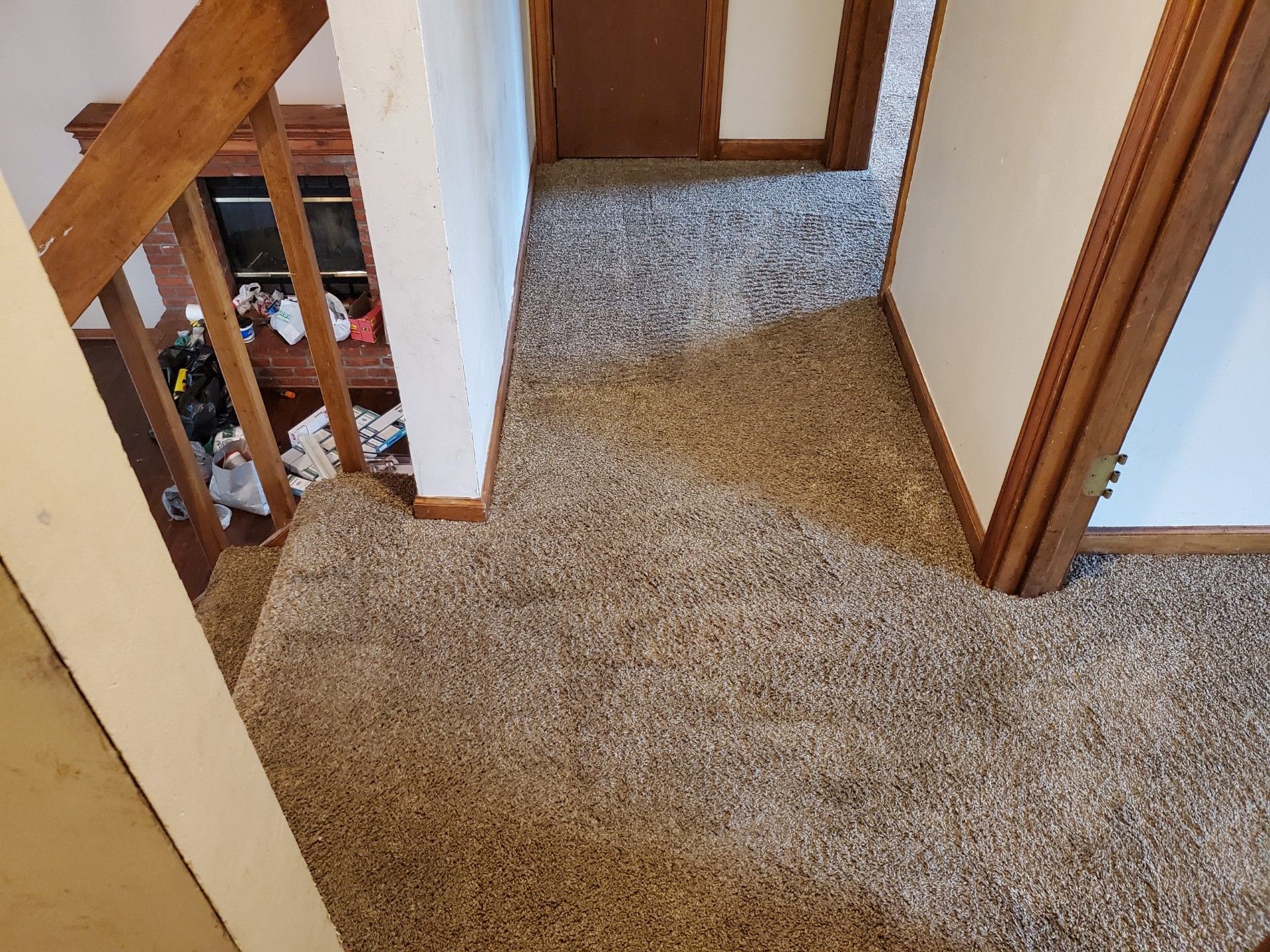 Top-down view of a carpeted hallway with a staircase and a doorway at the end.