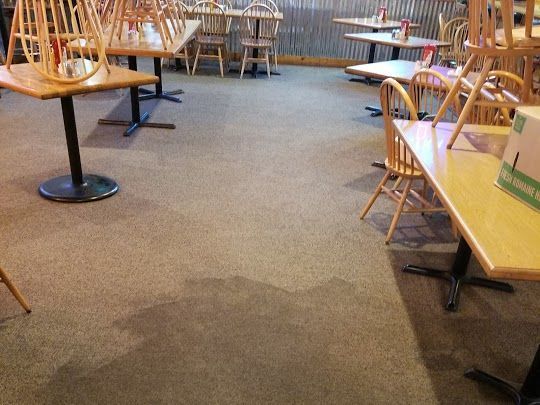Restaurant interior with tables, chairs, and speckled flooring. Some chairs are upside down on tables.
