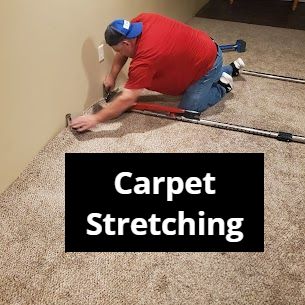 Person stretching carpet with tools near a wall.