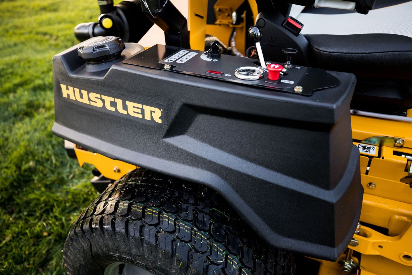 Close-up of a Hustler lawn mower’s black side compartment on yellow machinery outdoors