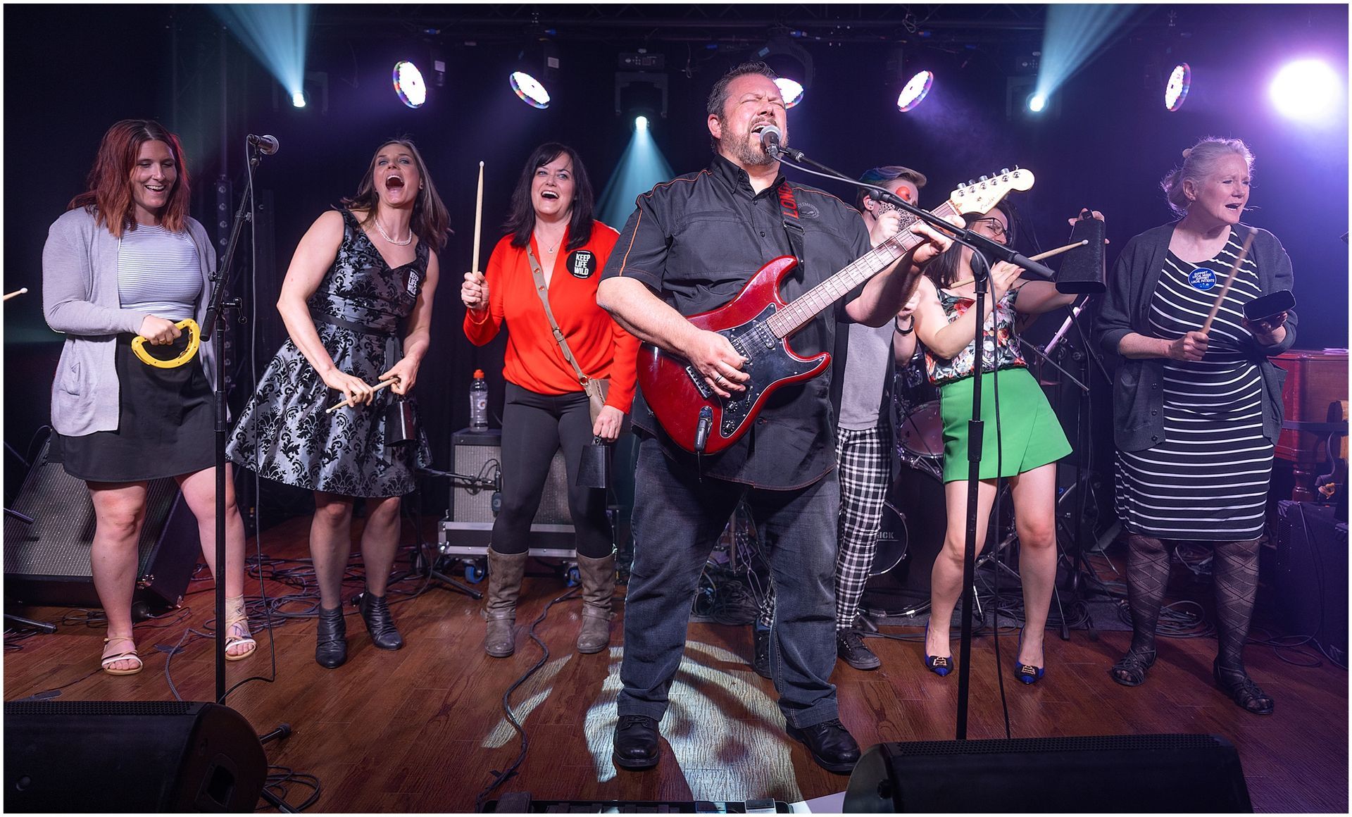 Band performing on stage: Guitarist singing, backing vocalists, lights.