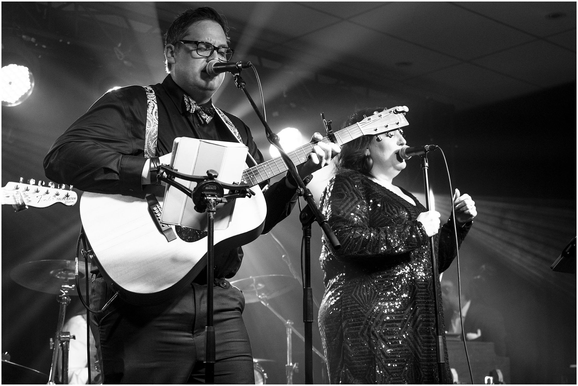 Two musicians performing on stage: man plays guitar and button accordion; woman sings.