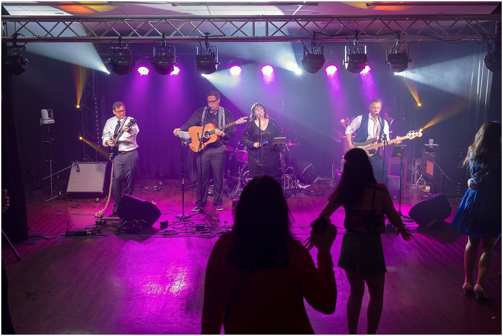 Band performing on stage under purple and white lights, with people dancing in the foreground.