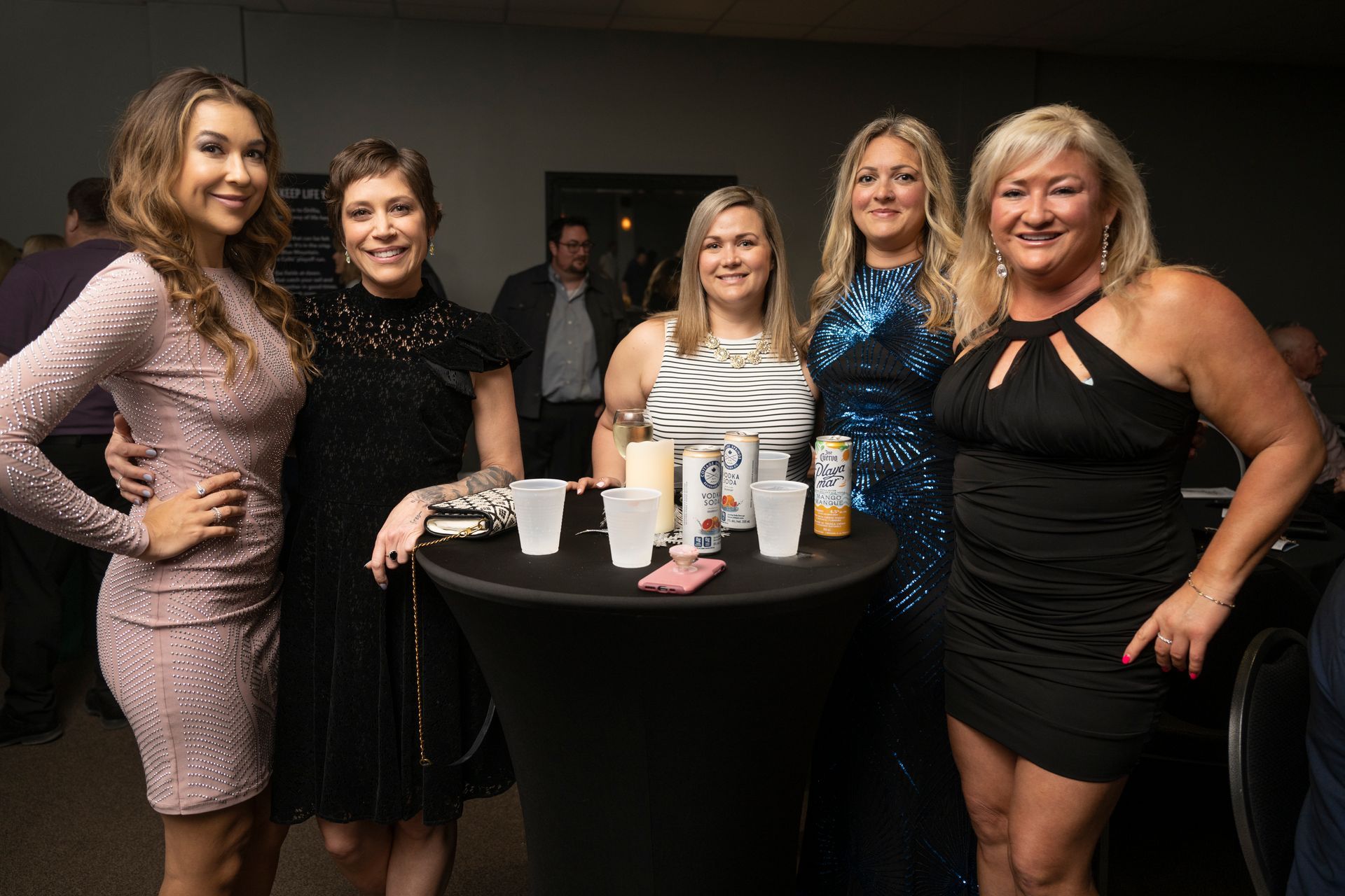 Five people posing near a small table with drinks in a room.