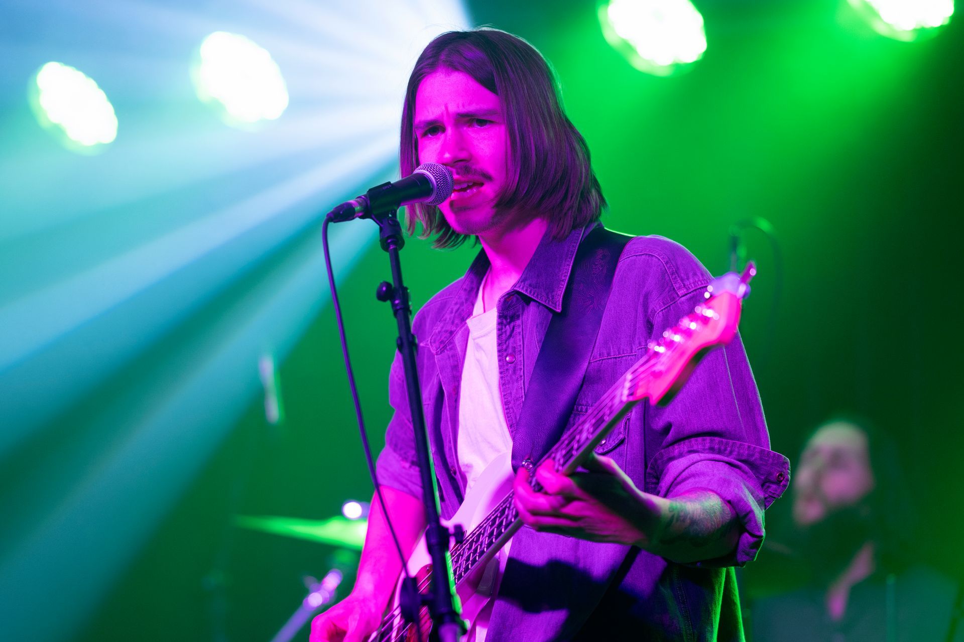 Man playing guitar and singing on stage under green and purple lights.