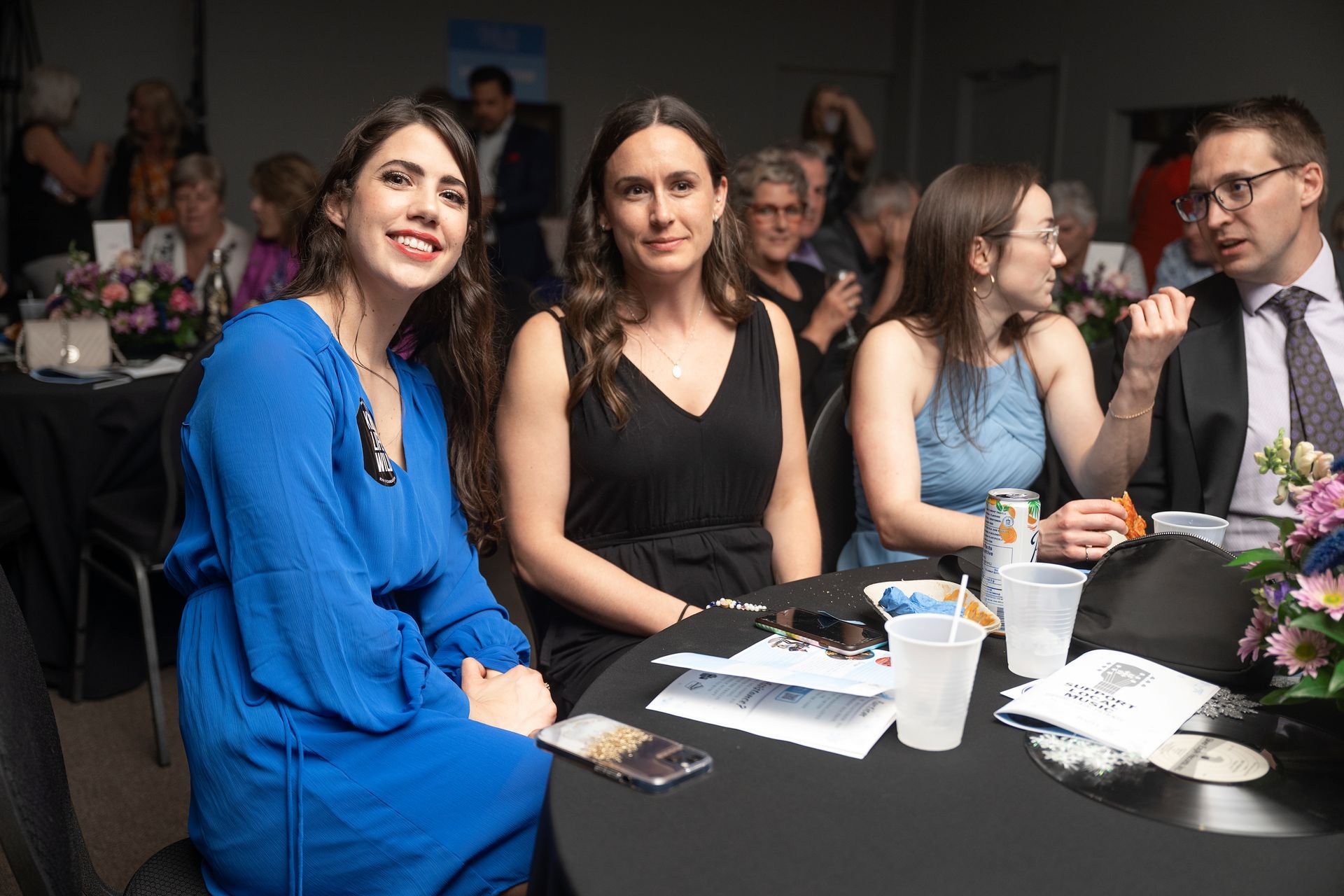 Four people seated at a round table, possibly at an event. Woman in blue smiling, others looking at the viewer.