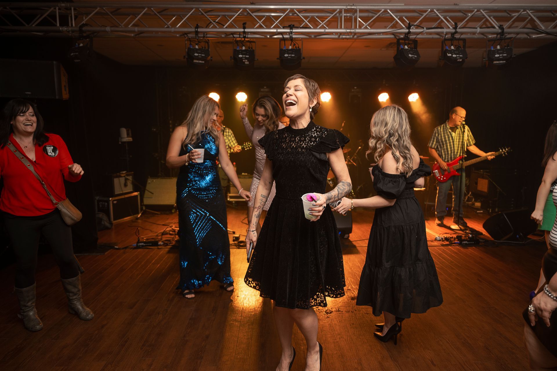 People dancing and singing at a concert in a dimly lit venue with a band on stage.