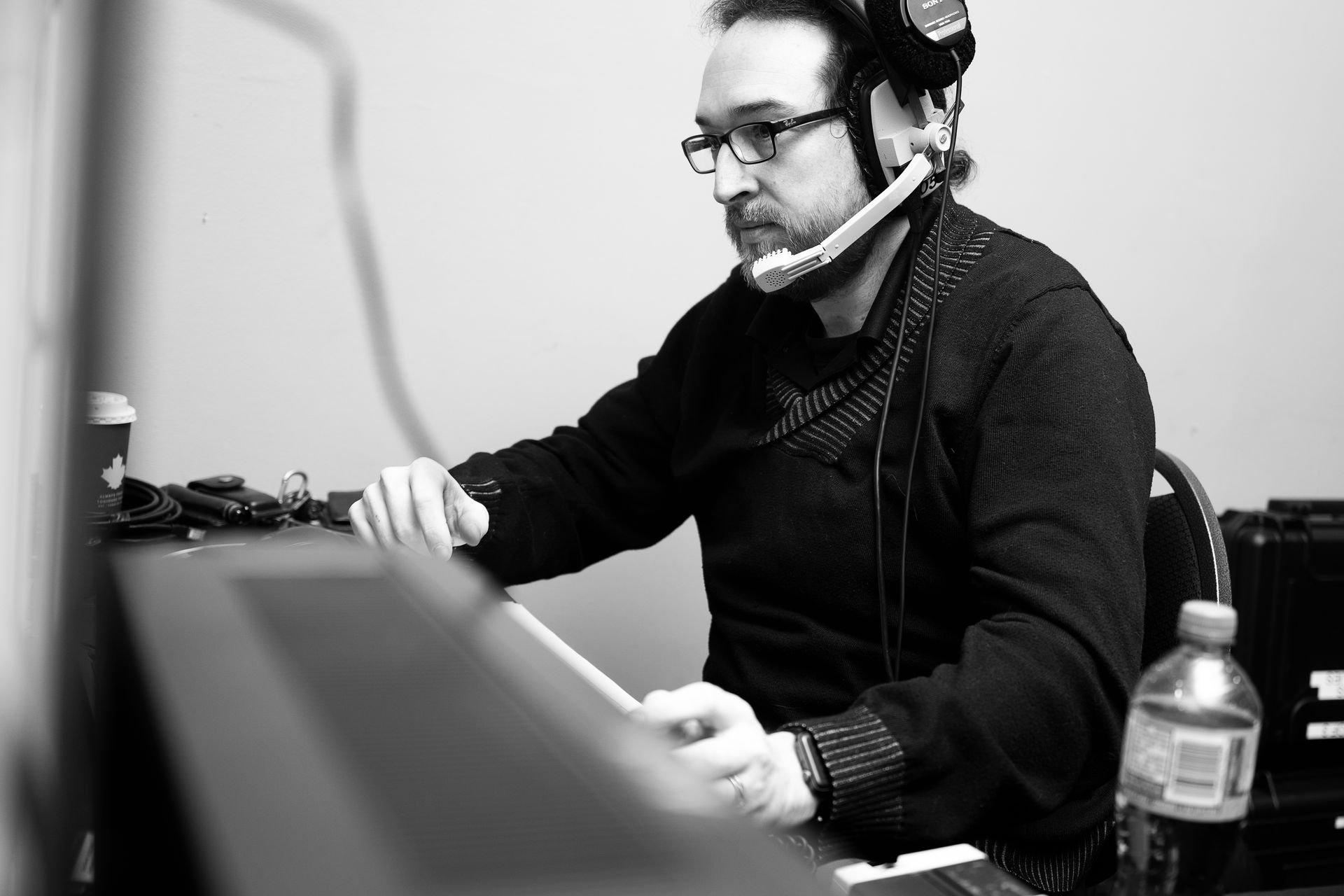 Man wearing glasses and headset, operating equipment, indoors.