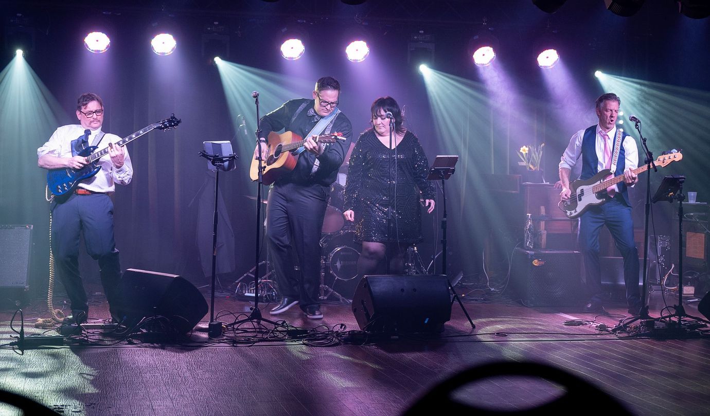 two musicians playing a song together. lights are shinning behind them. Microphone stands and instruments are on stage.