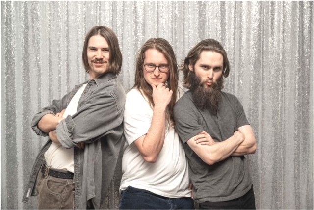 Three people posing in front of a sparkly silver backdrop. All have long hair, crossed arms, and various expressions.