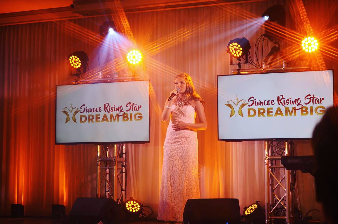 Woman in gown singing on stage with screens displaying 