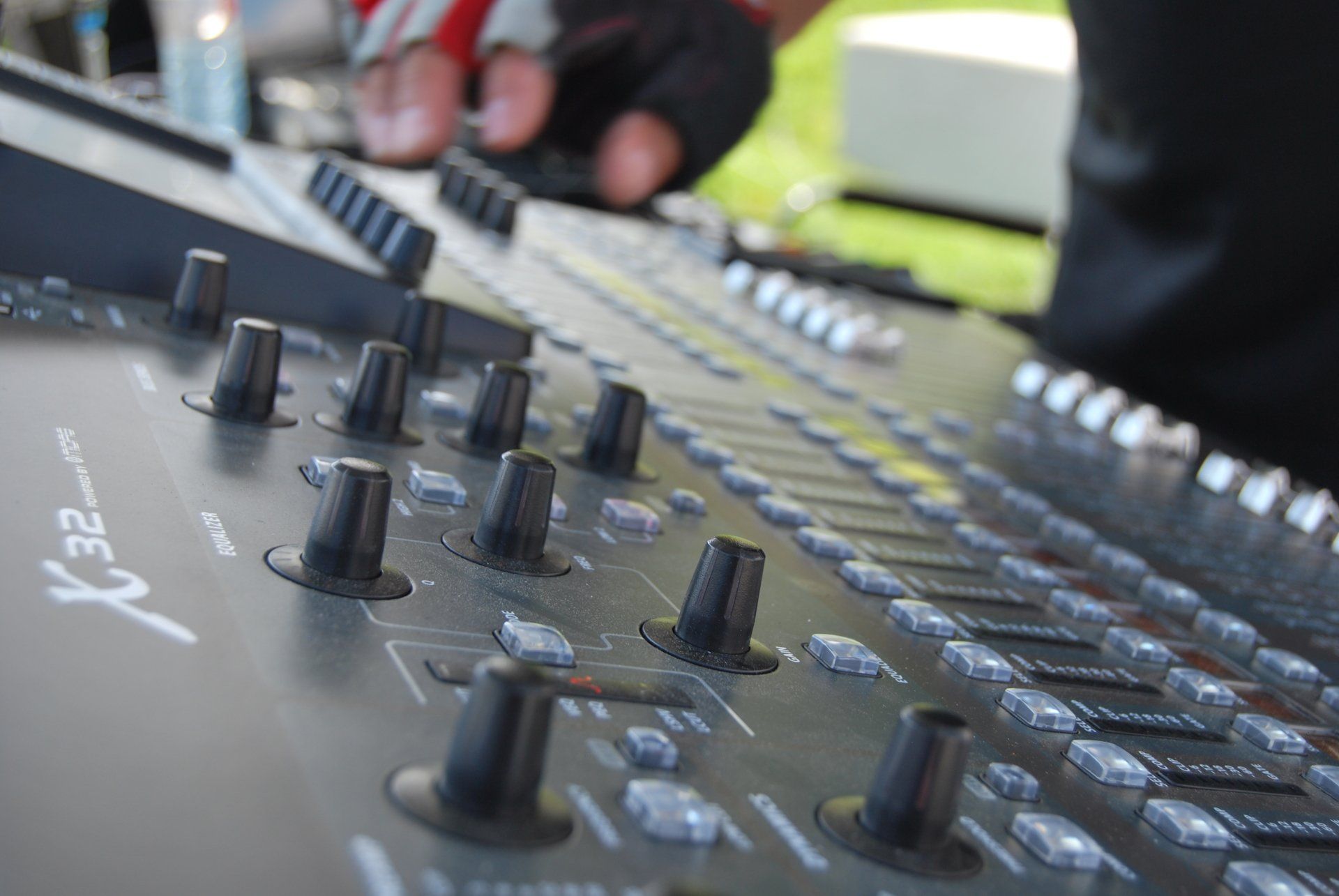 Close-up of a black Behringer X32 mixing console with knobs and faders. A hand adjusts a knob.