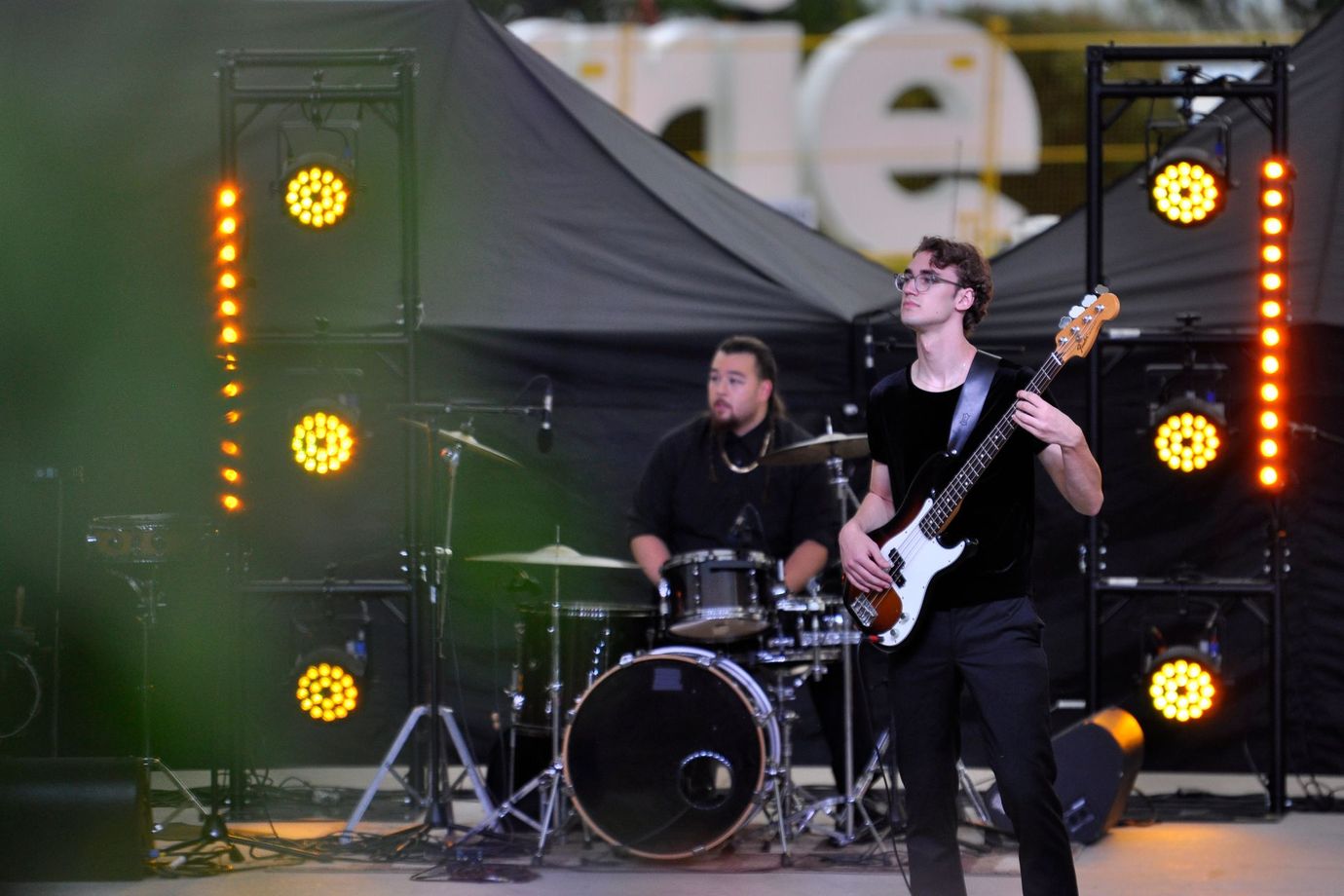 two musicians on a stage in downtown Barrie. One is holding a guitar and one is sitting behind a drum set.