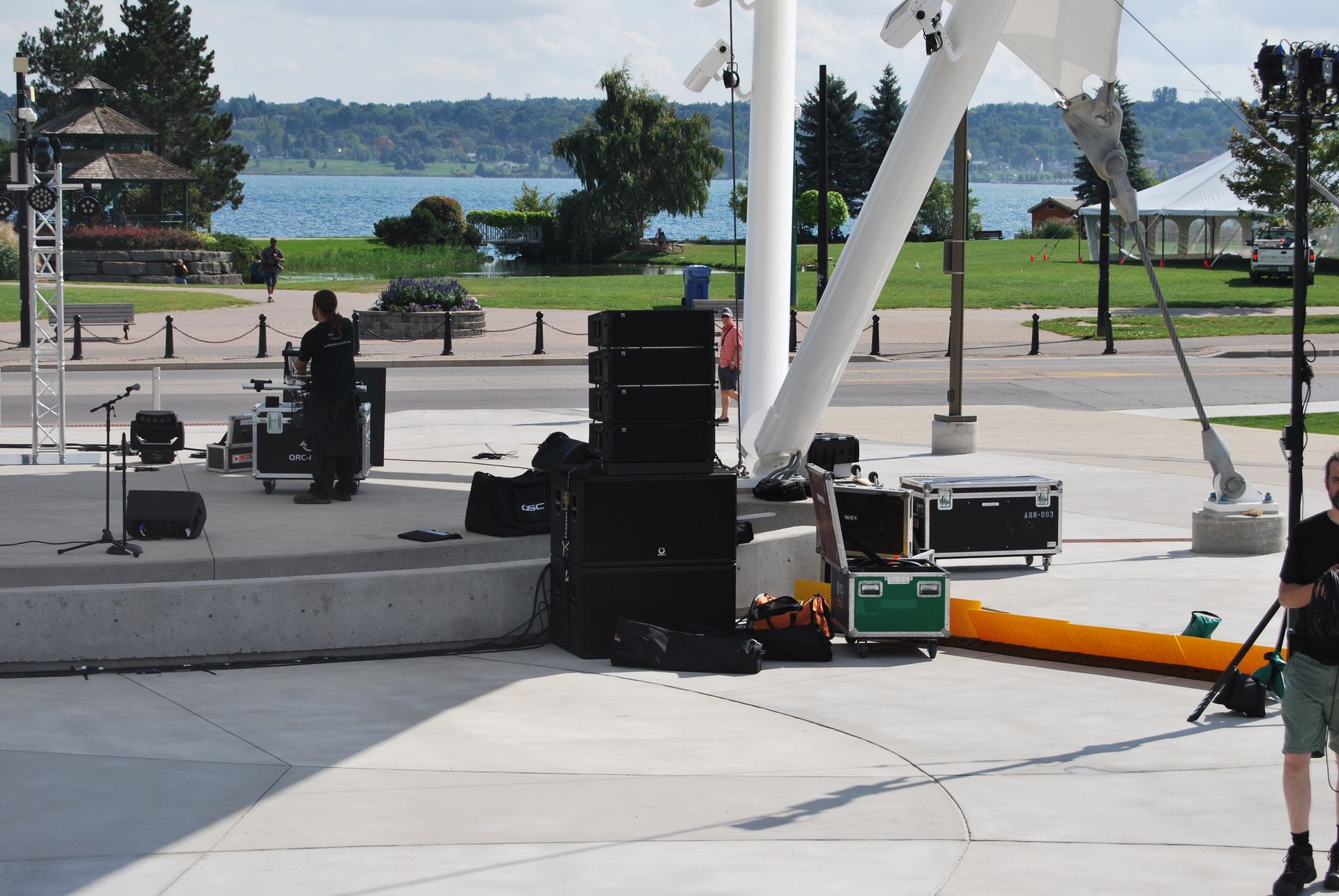 Man on stage sets up sound equipment near a waterfront.