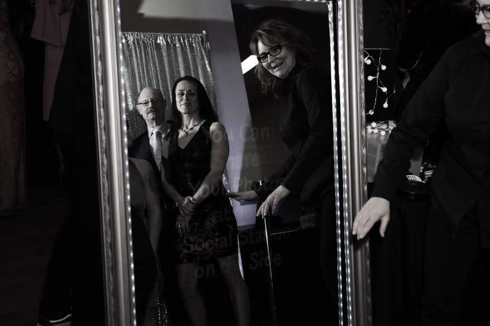 People posing in front of a photo booth mirror, woman taking photo. Black and white.