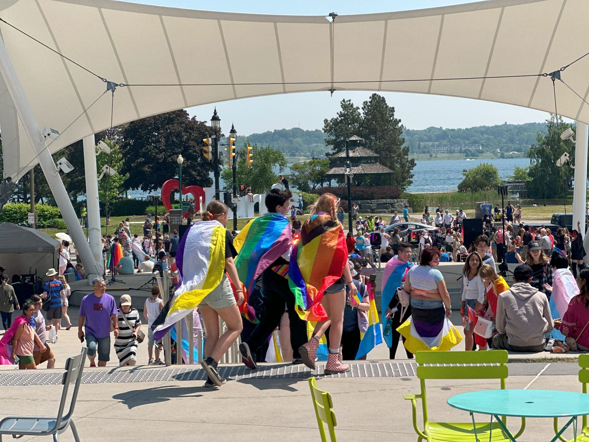 People with rainbow flags walking toward a crowd at an outdoor Pride event.