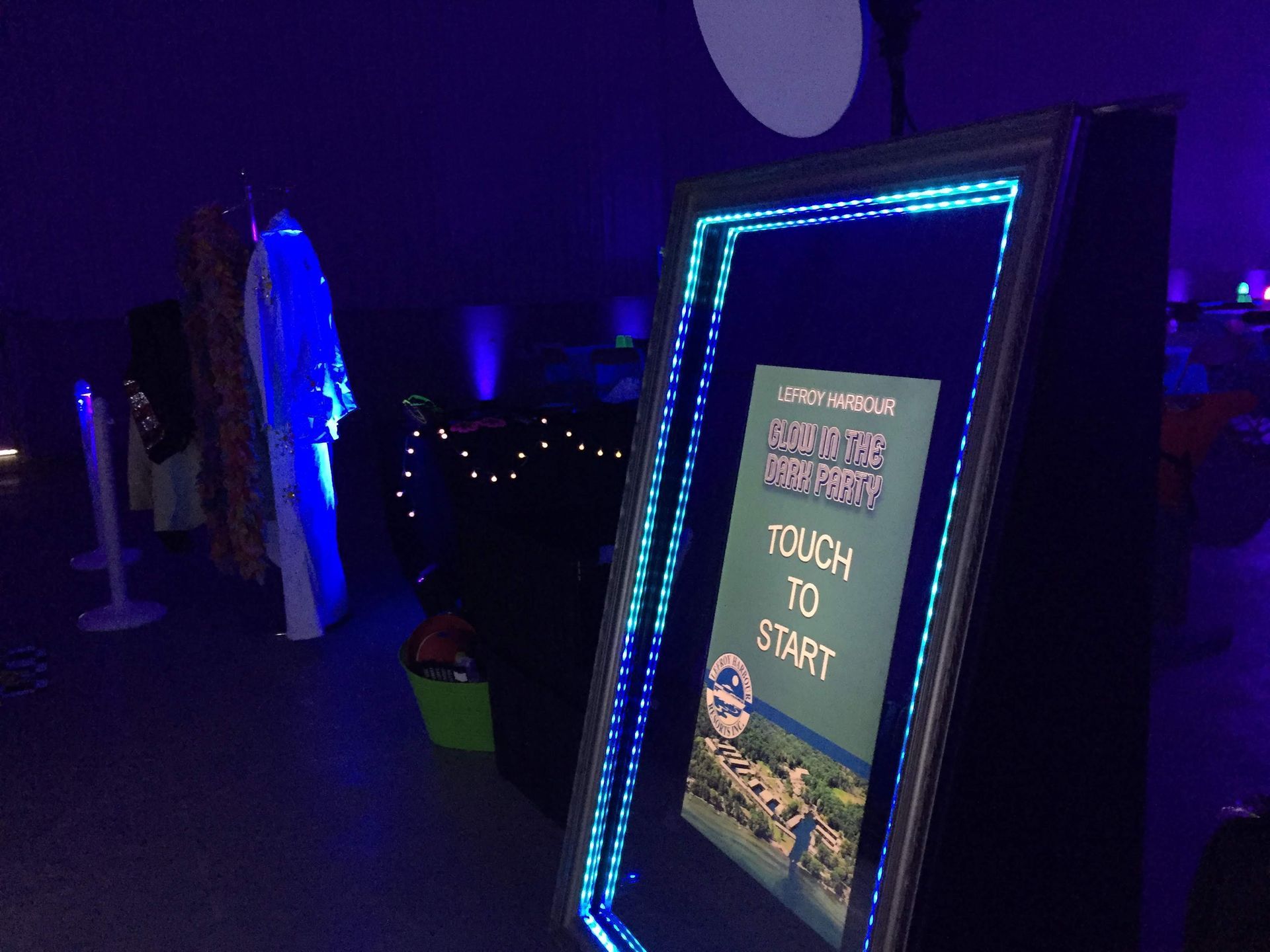 A photo booth mirror with blue LED lights, indoors. The screen says 