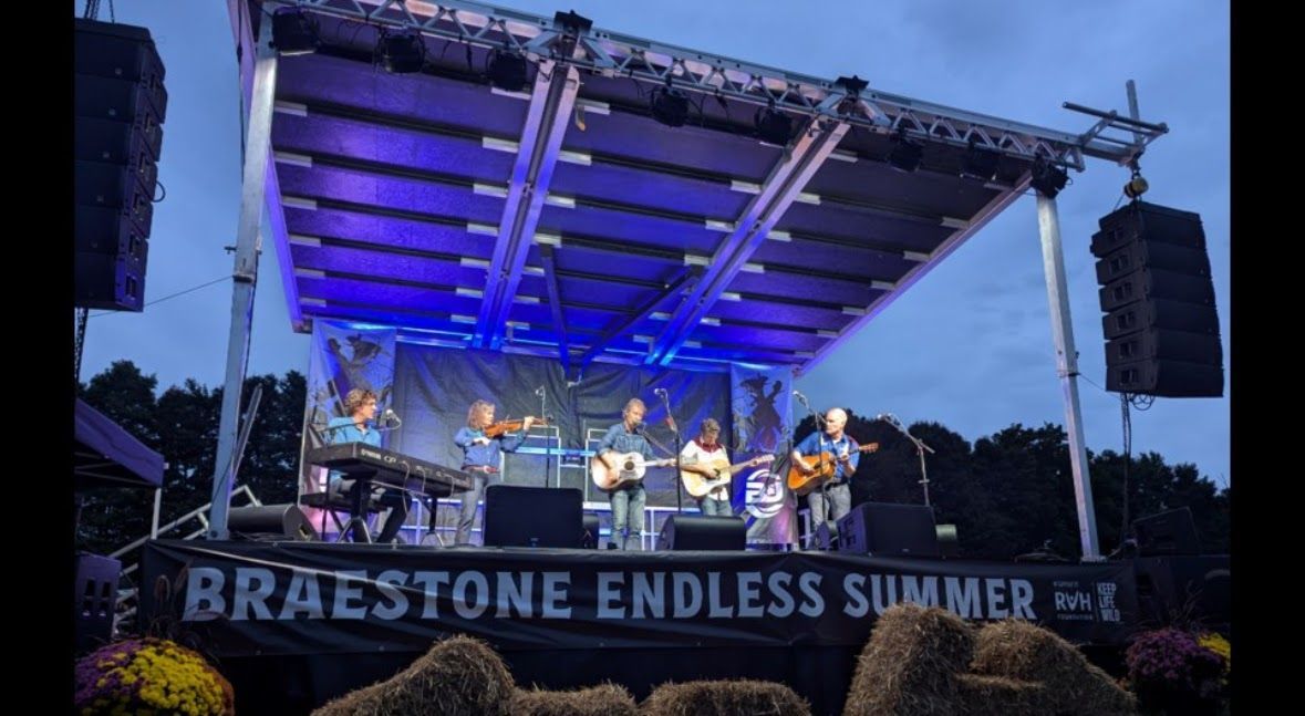 Live band on a SL100 mobile stage. the image is taken at dusk. there is a sign running along the front of the stage.