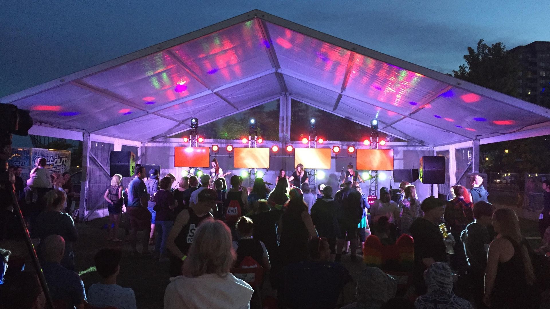 People dancing under a tent at night with stage lights and screens.