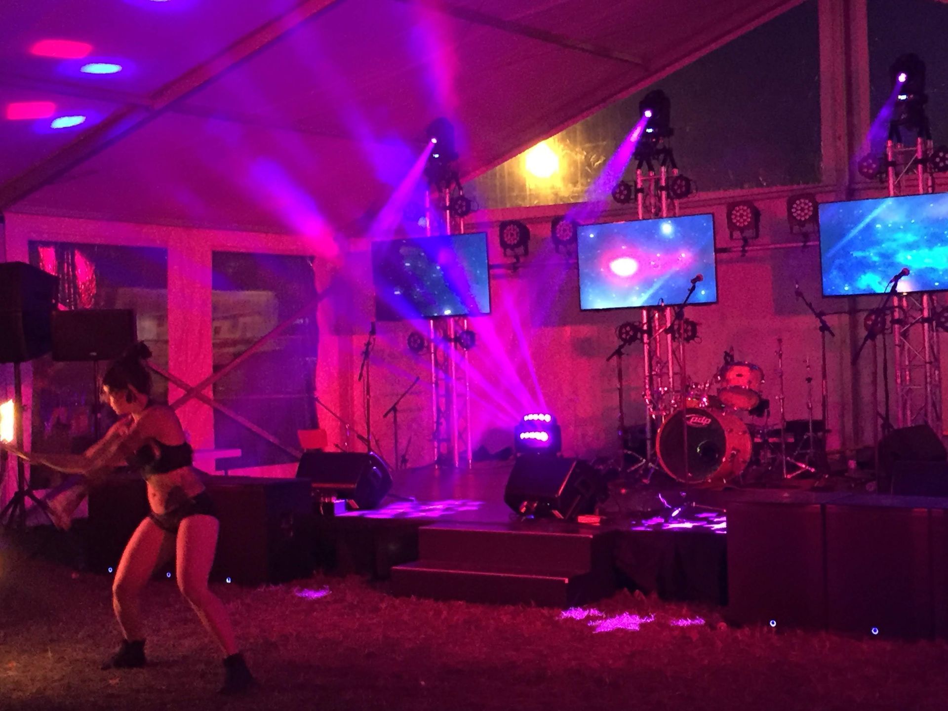 A woman dances onstage under purple stage lights with screens and a drum set.