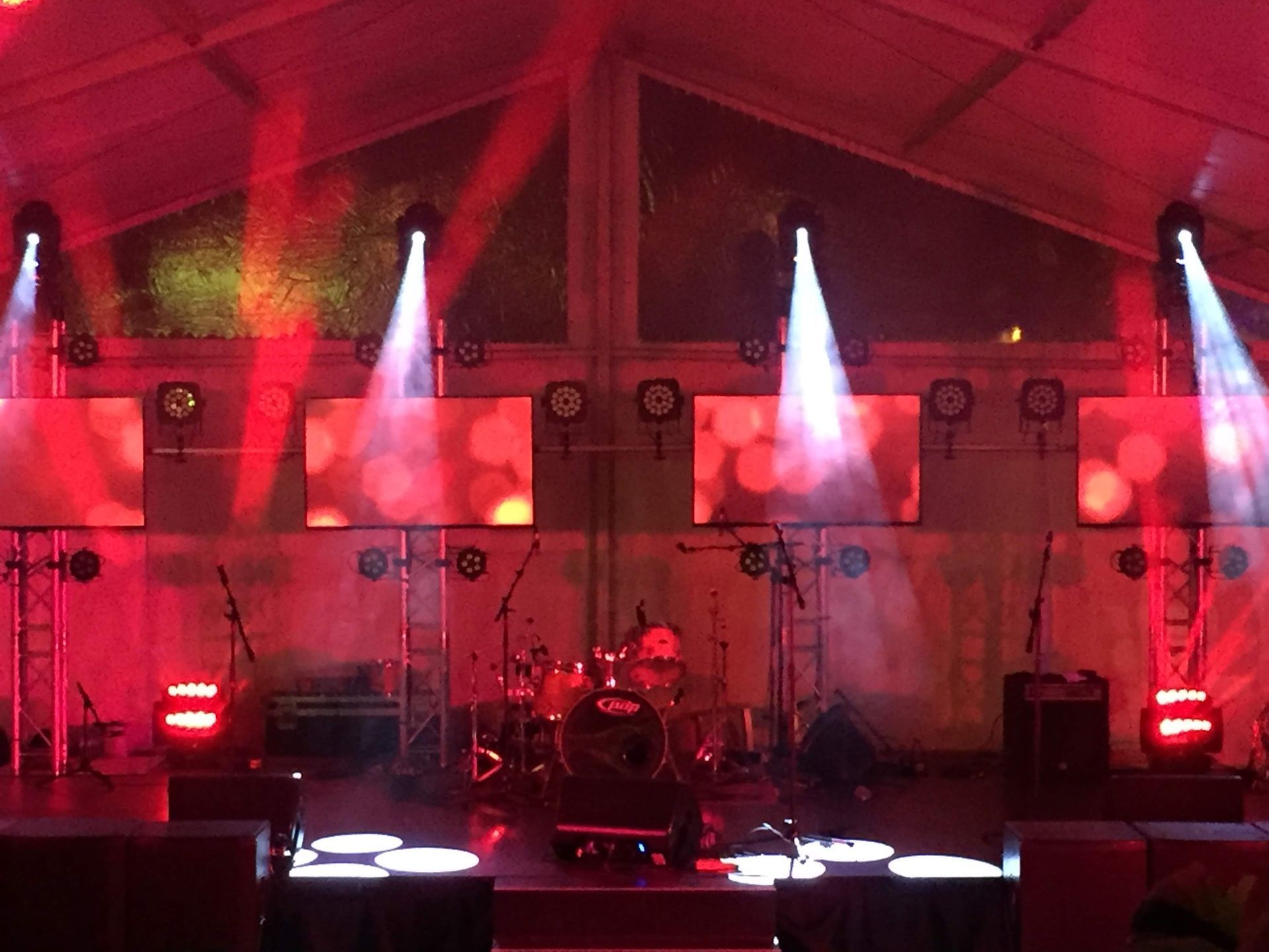 Stage lit with red and white spotlights. A drum set and microphones are set up for a performance.