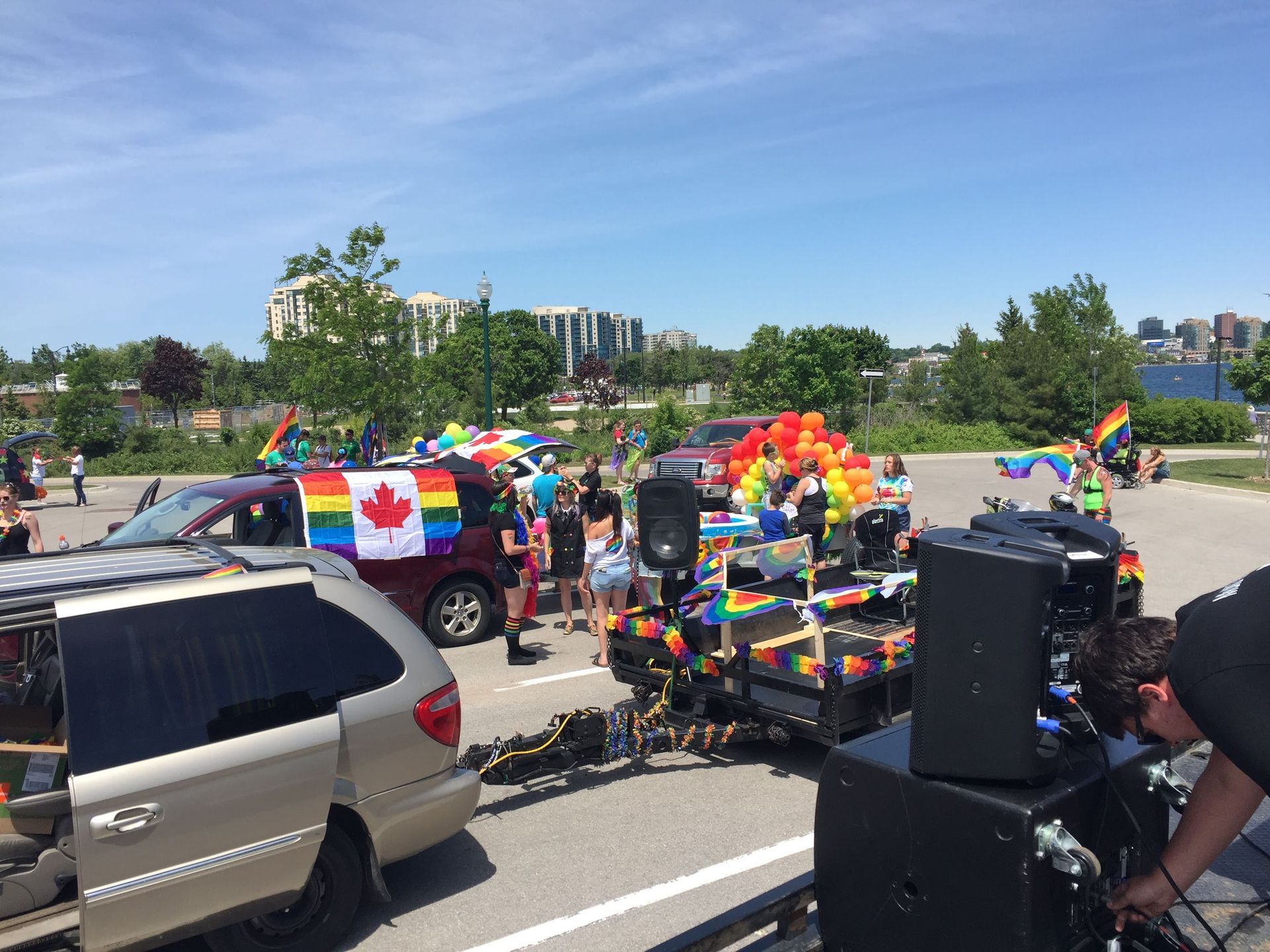 Cars decorated with rainbow flags and balloons at a Pride event, with a sound system in the foreground.
