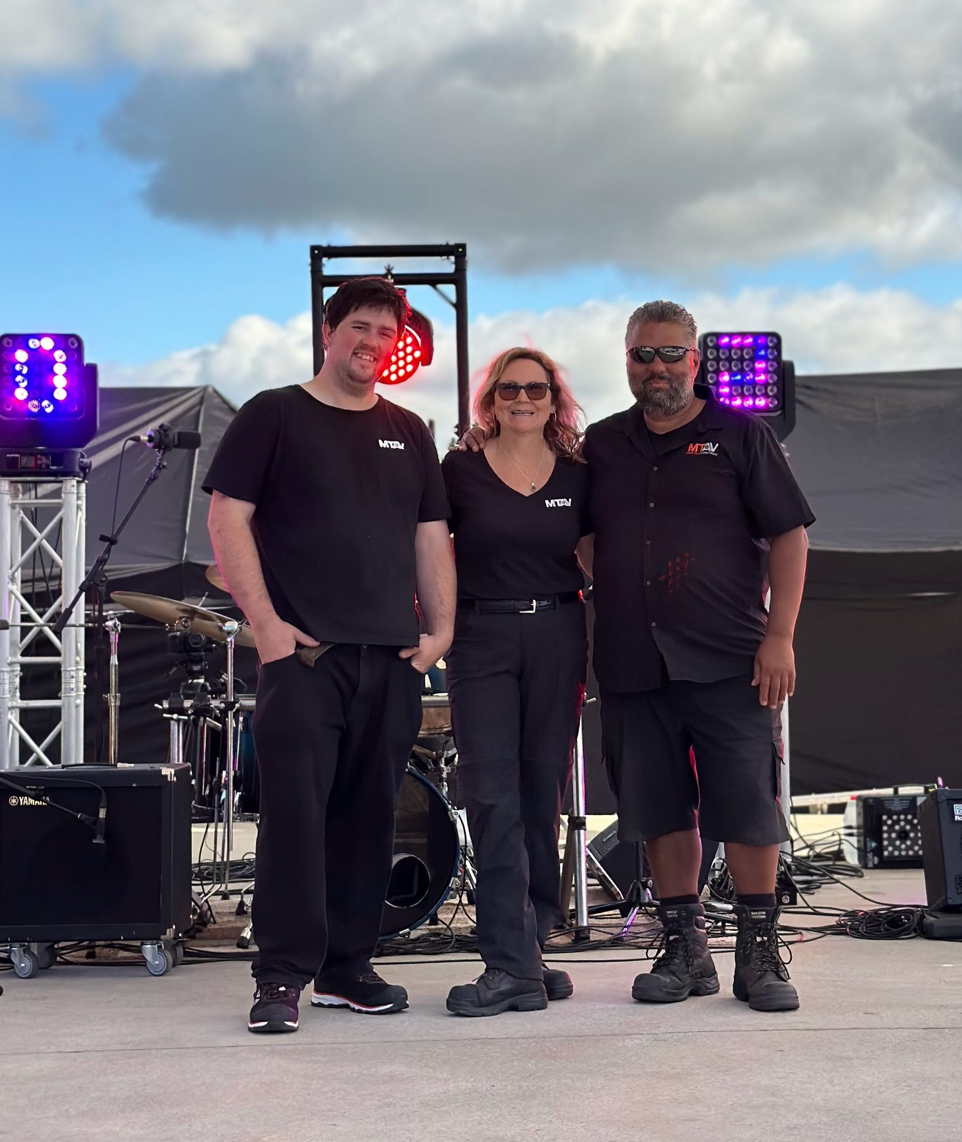 Three people on a stage in front of lighting equipment. All are wearing black and smiling.