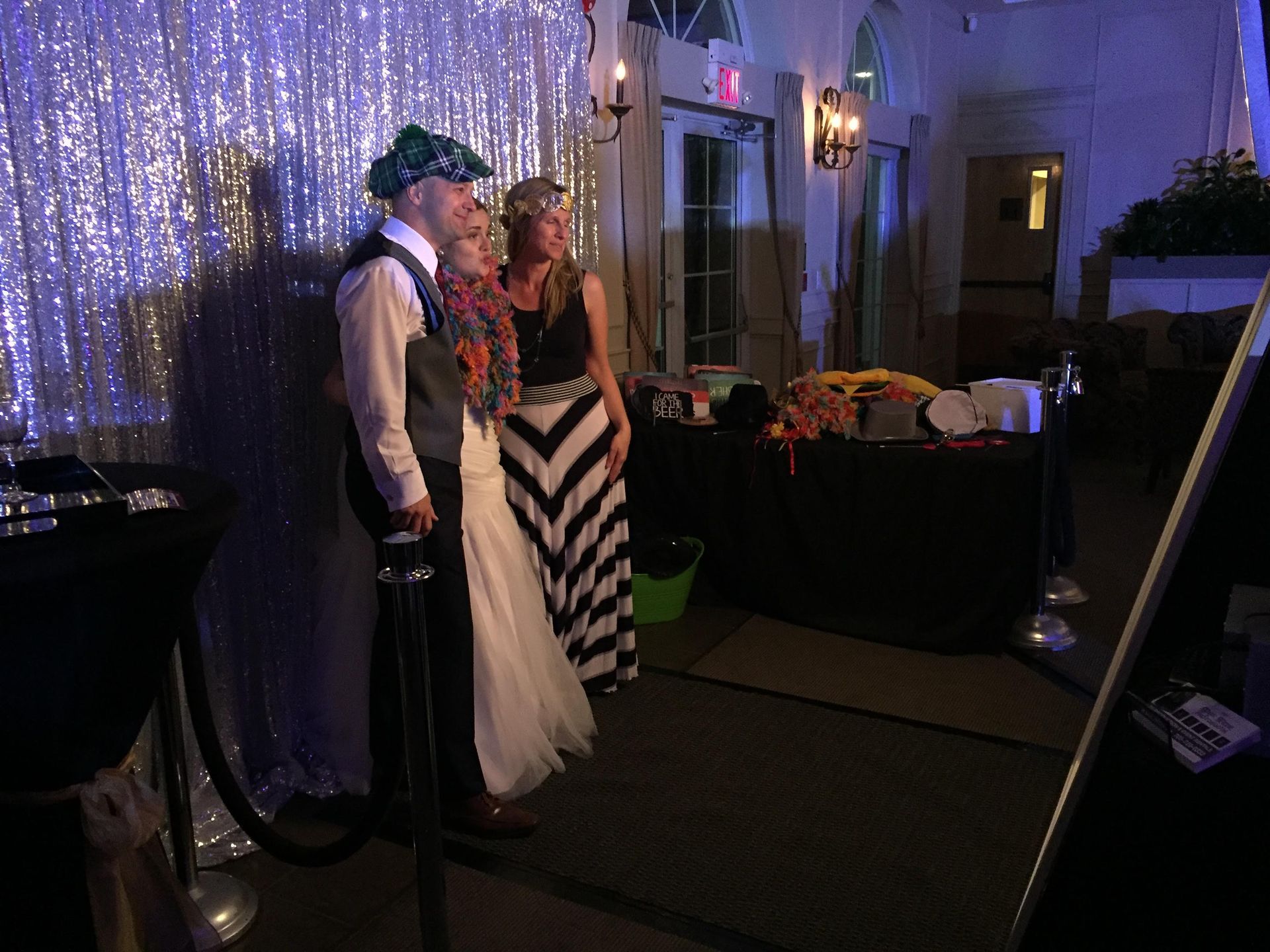Couple poses at a photo booth with accessories, silver backdrop, dimly lit event.