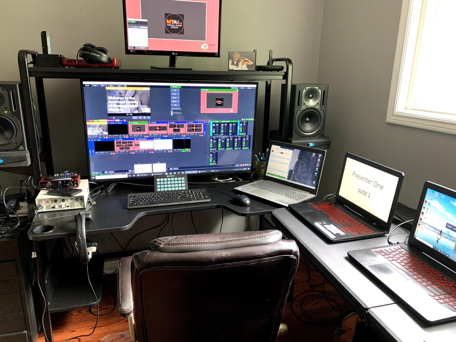 A desk with multiple laptops, monitors, speakers, and streaming equipment in a room.