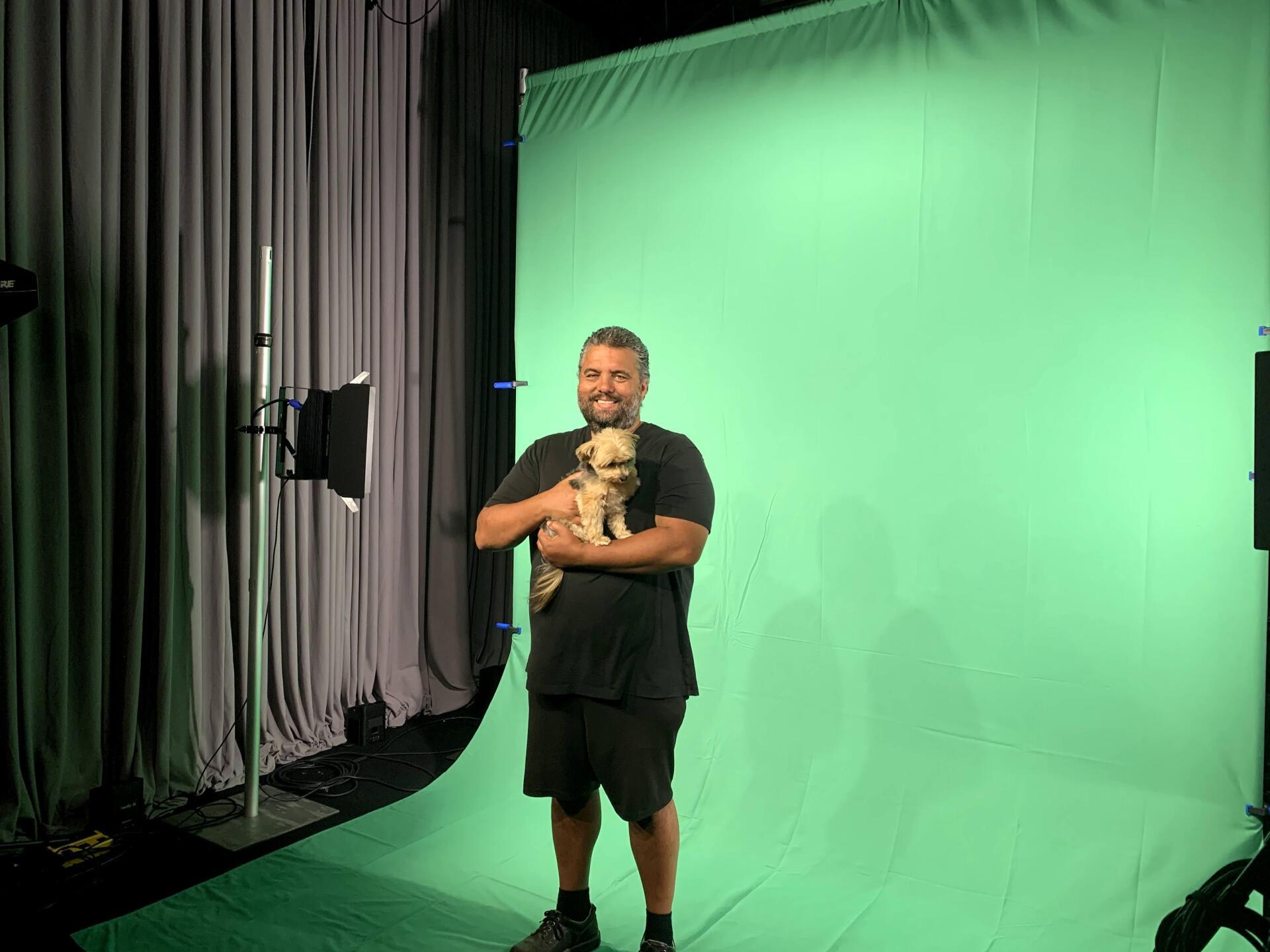 Man holding puppy in front of a green screen; studio setting with lighting and curtains.