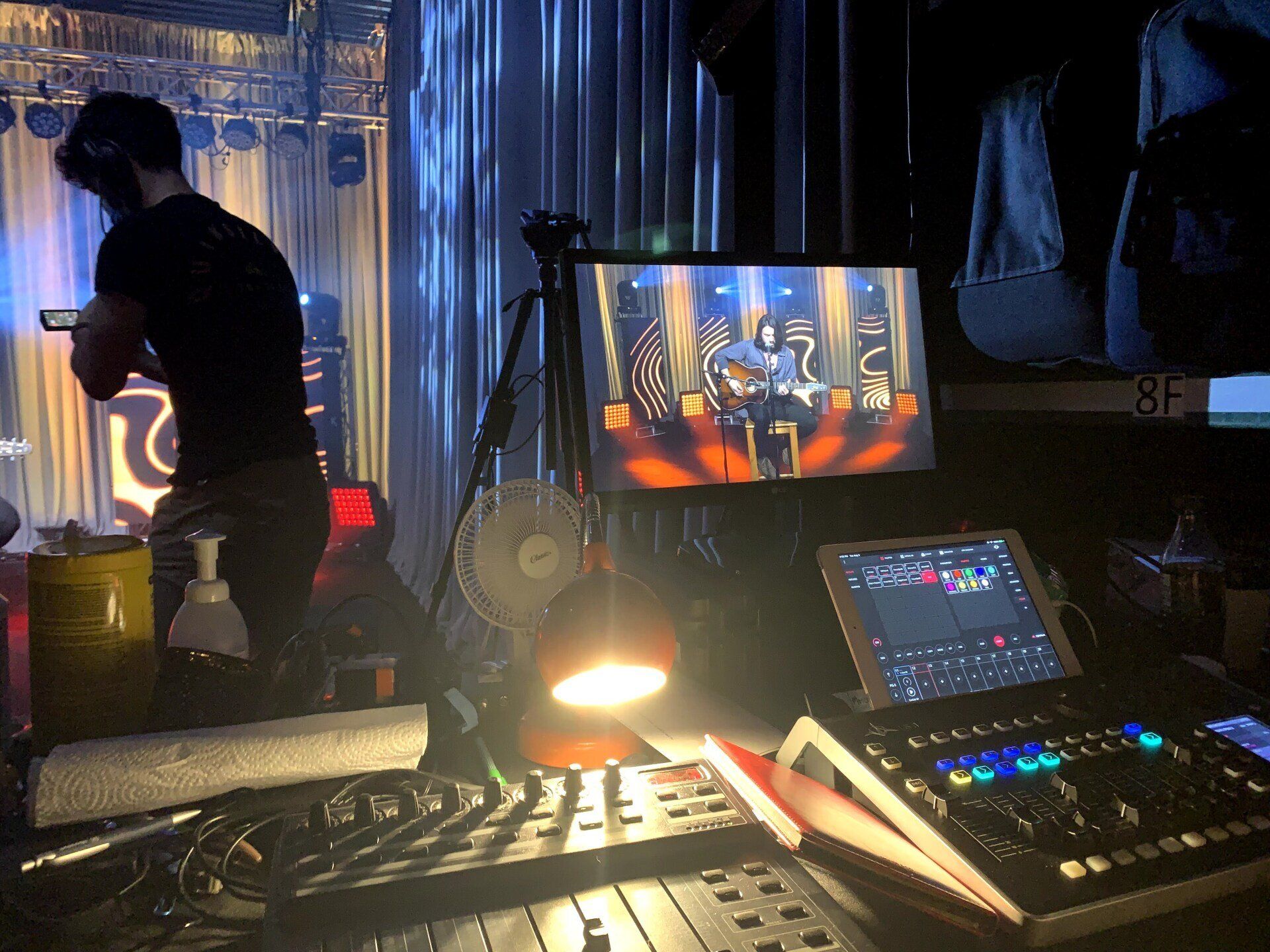 A person monitors a live stream feed of a musical performance in a dimly lit venue.