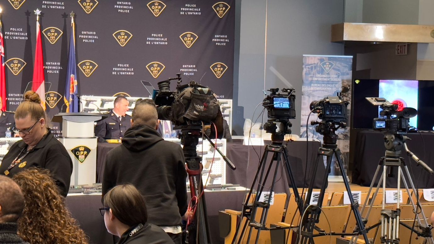 Many media cameras set up in a room with a table and OPP officer sitting at it ready for a press conference.