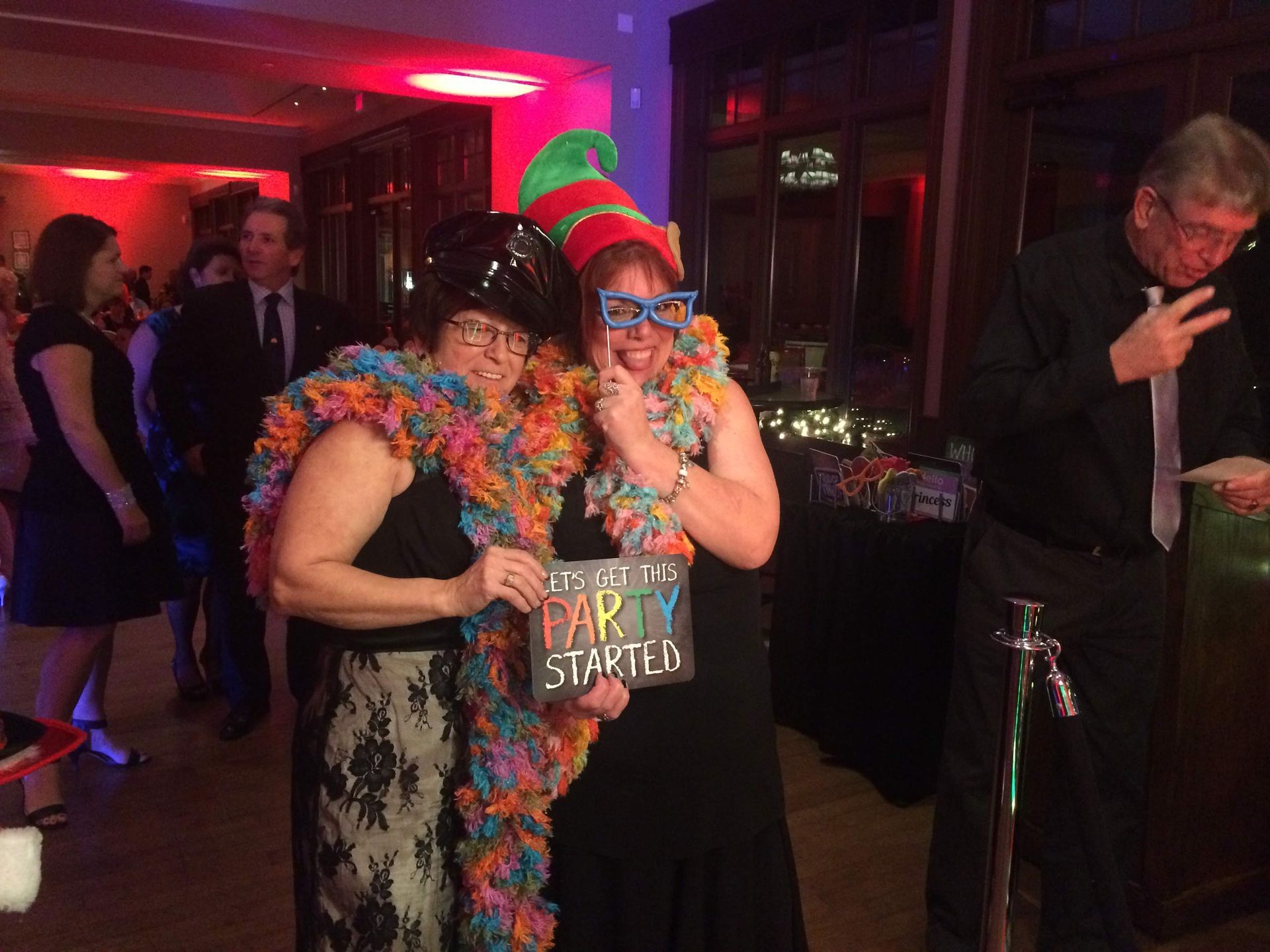 Two women pose at a party, holding a sign that says 