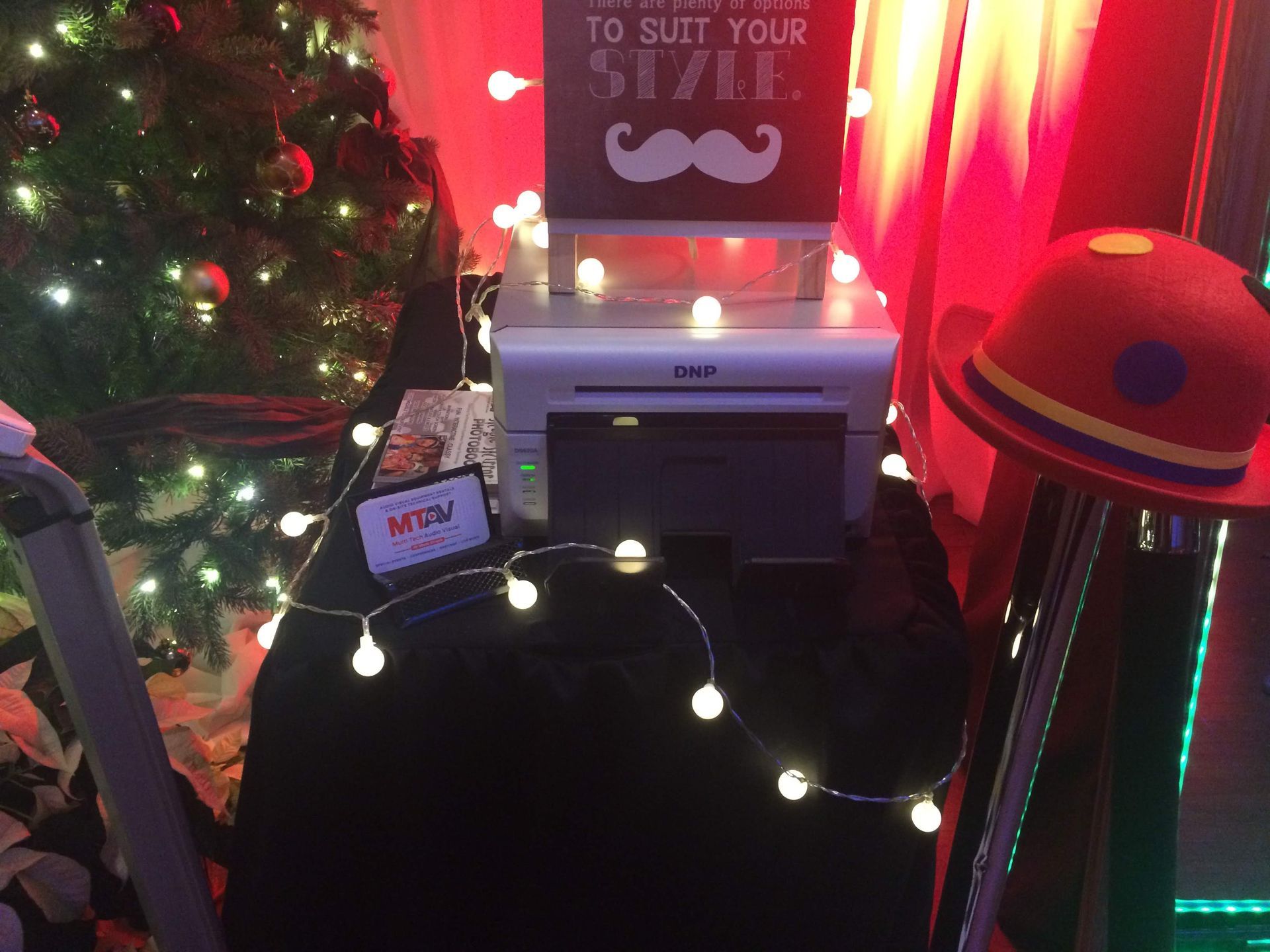 Christmas photo booth setup with a printer, string lights, props, and a sign.
