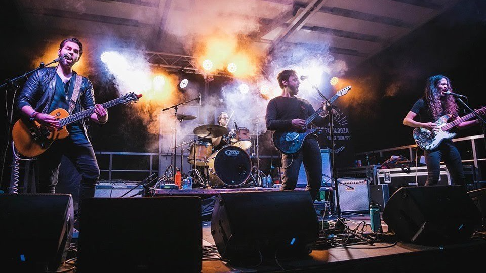 Band performing on stage with guitars, drums, and lighting.