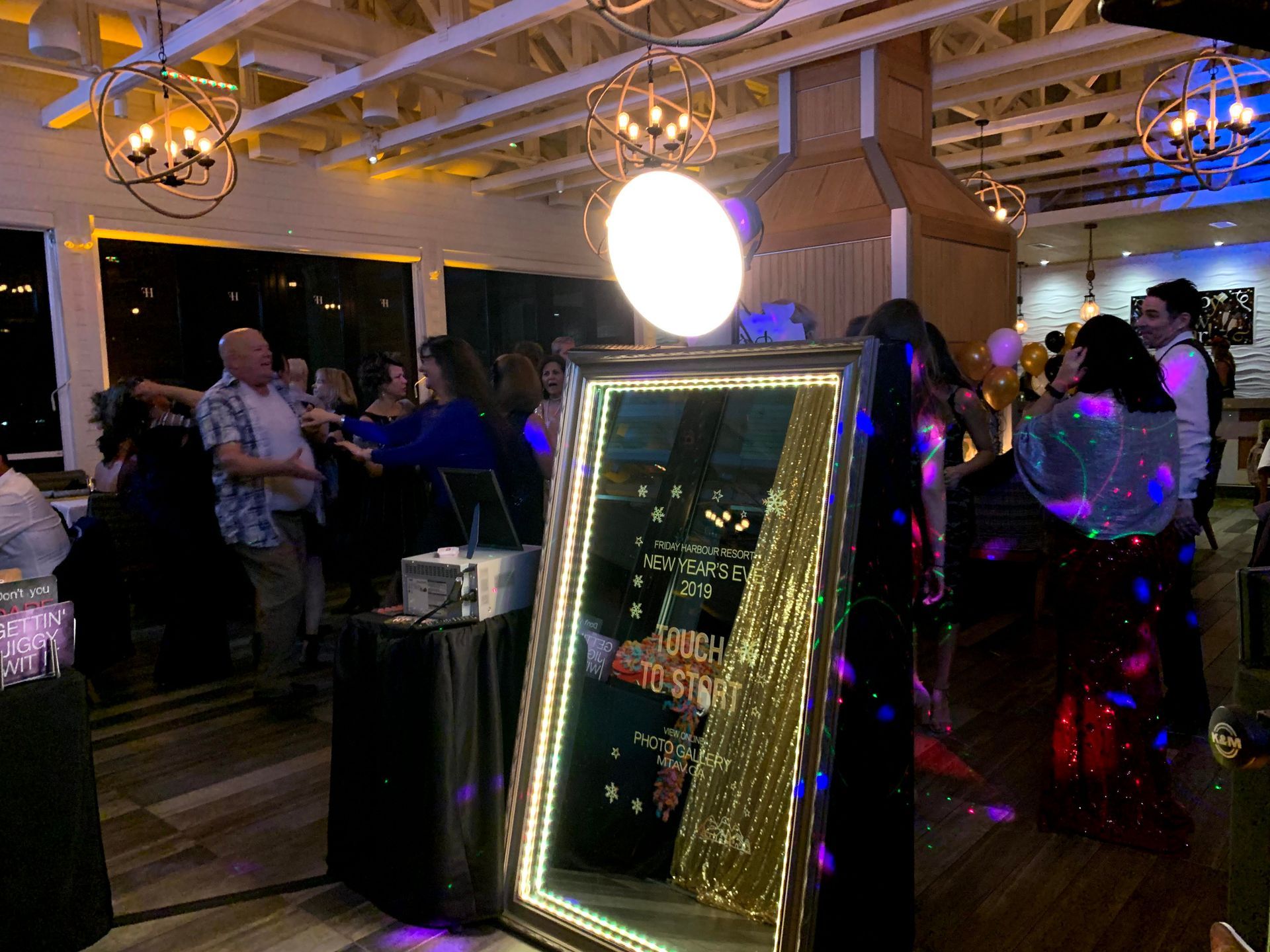 Party with a photo booth mirror, disco lights, and people dancing in a well-lit venue.