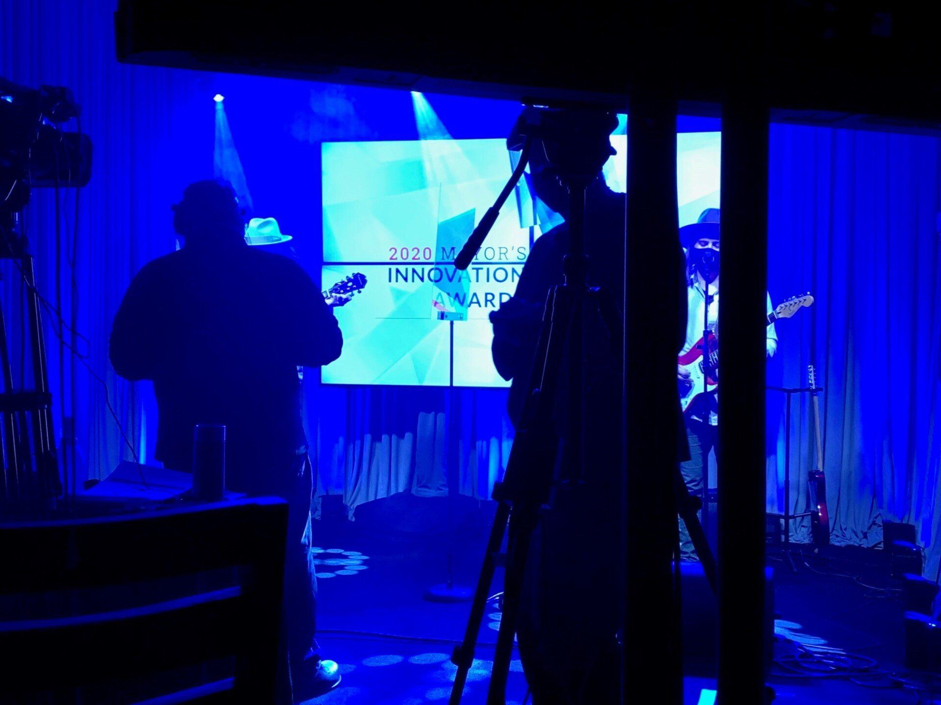 Band performing on stage, bathed in blue light. A screen displays 