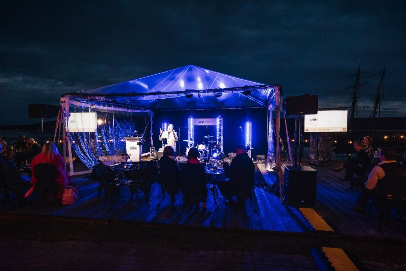 Stage with band performing at night under blue lights. Audience visible.