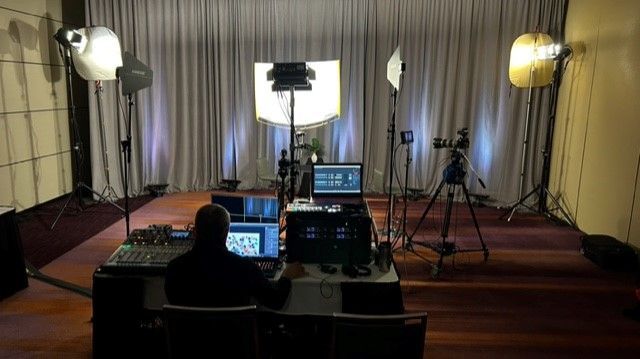 Filming studio setup with lights, cameras, and person operating a console in front of a backdrop.
