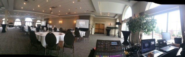 An event hall with round tables, chairs, and AV equipment. Large windows provide natural light.